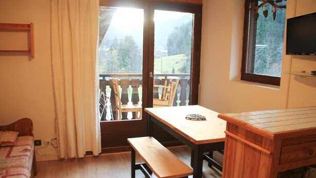 A room with a wooden table, bench, and a small TV on the wall.