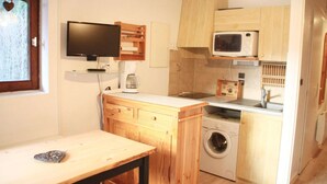 A compact kitchen with a washing machine, a microwave, and a television on a wooden cabinet.