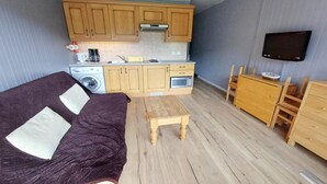 A compact living space with a kitchenette, a sofa, a small wooden table, and a TV mounted on the wall. - Apartment in Chatel for two people (Châtel)