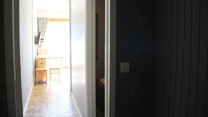 A narrow hallway with a wooden floor leading to a room with a bed and a window. - Apartment in Chatel for two people (Châtel)