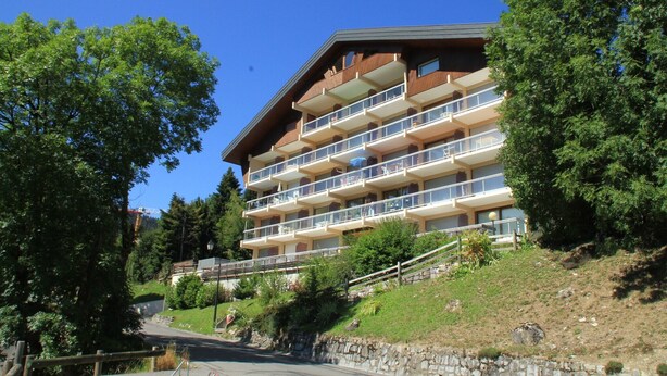 A multi-story hotel with balconies, set on a hillside with trees and a clear sky. - Apartment in Chatel for two people (Châtel)