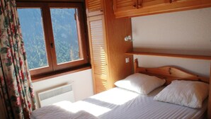 A single bed with white bedding in a room with wooden furniture and a window with curtains. - Apartment in Petit Châtel near Cable Car (Châtel)