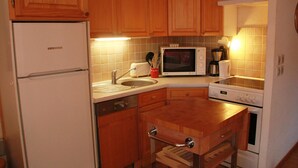 A compact kitchen with wooden cabinets, a built-in microwave, a sink, and a stove. - Apartment in Petit Châtel near Cable Car (Châtel)