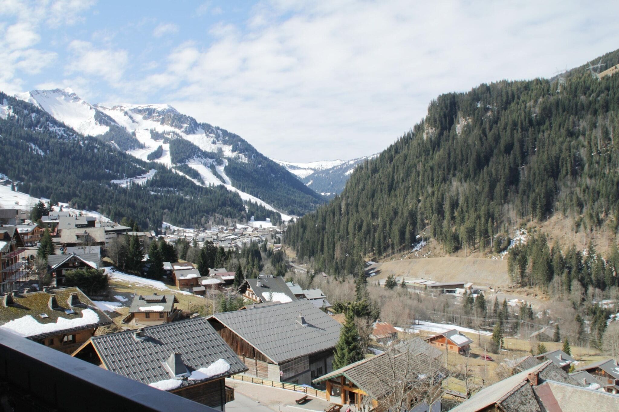 A mountainous village with snow-covered peaks, dense forests, and traditional wooden buildings.