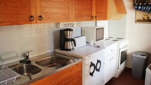 Une cuisine compacte dotée d’armoires en bois, d’un four à micro-ondes, d’une machine à café et d’une poubelle.