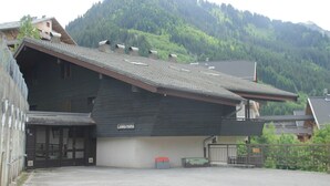 A building with a sloped roof, a sign reading "L'ANNA MARIA," and a view of a forested mountain in the background.