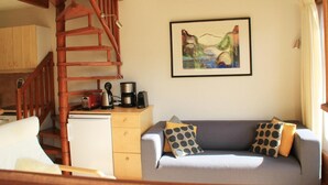Un accogliente soggiorno con una scala in legno, un divano con cuscini decorati, una macchina da caffè e un quadro appeso al muro.
