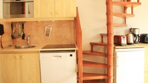Una cucina compatta con mobili in legno, forno a microonde integrato, lavastoviglie e un piccolo frigorifero.