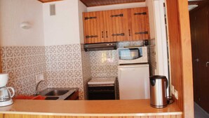 Una cocina pequeña con baldosas estampadas, armarios de madera, microondas, hervidor y cafetera.