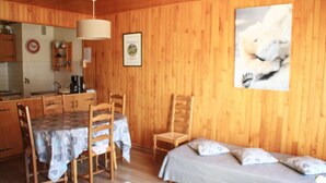 A wooden interior with a dining table, chairs, a bed, and a polar bear picture on the wall.
