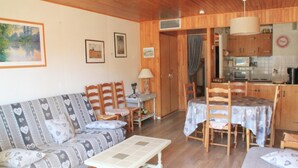 A cozy living room with a sofa, chairs, a small table, and a kitchen area with wooden cabinets and a dining table.