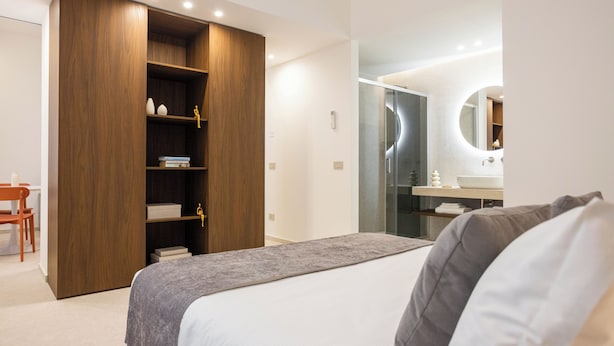 A modern bedroom with a bed, a wardrobe, a desk, and a bathroom with a mirror. - Nora's Suites (Palermo)