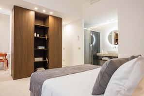A modern bedroom with a bed, a wardrobe, a desk, and a bathroom with a mirror. - Nora's Suites (Palermo)