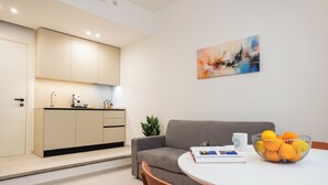 A modern kitchen with a grey sofa and a dining table with a fruit bowl and a coffee mug. - Nora's Suites (Palermo)