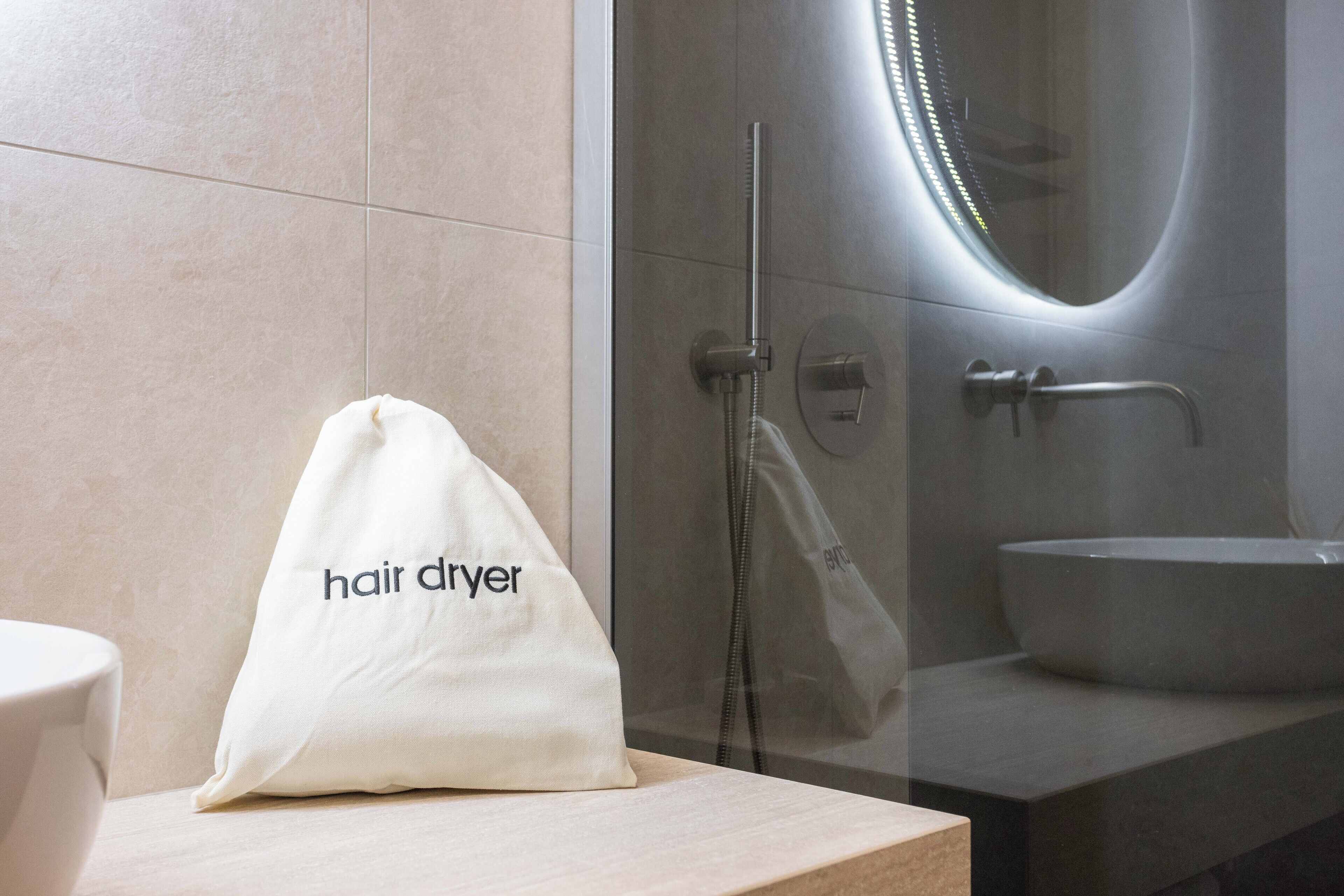 A bathroom with a white sink, a towel rack, and a white bag labeled "hair dryer" on a counter.