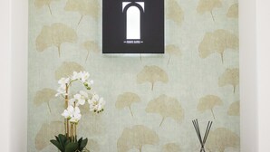 A reception area with a patterned wallpaper, a framed sign, a potted plant, and a small decorative item on a wooden cabinet. - Nora's Suites (Palermo)