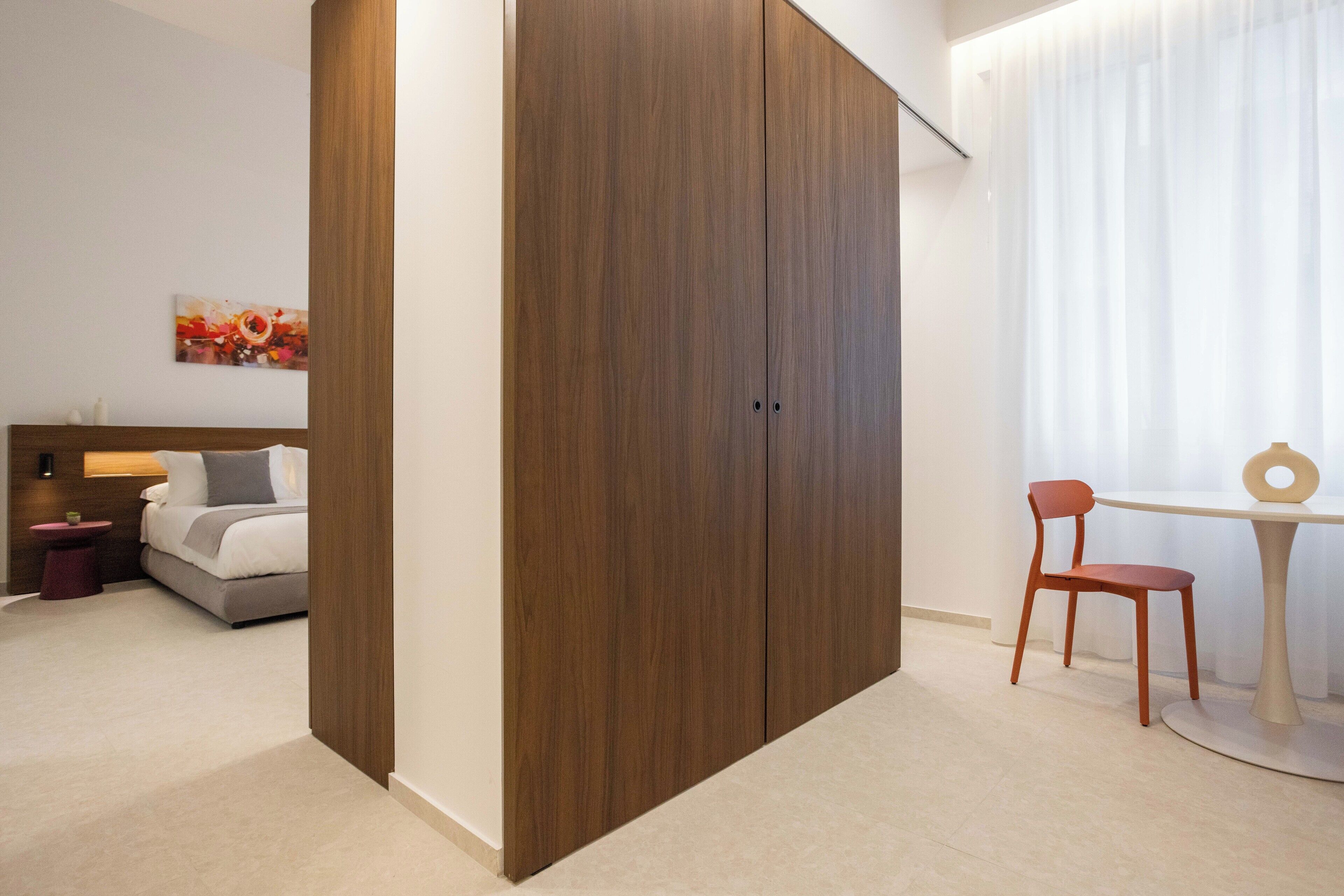 A bedroom with a bed, a wooden wardrobe, a bedside table, a chair, and a table with a ring on it.