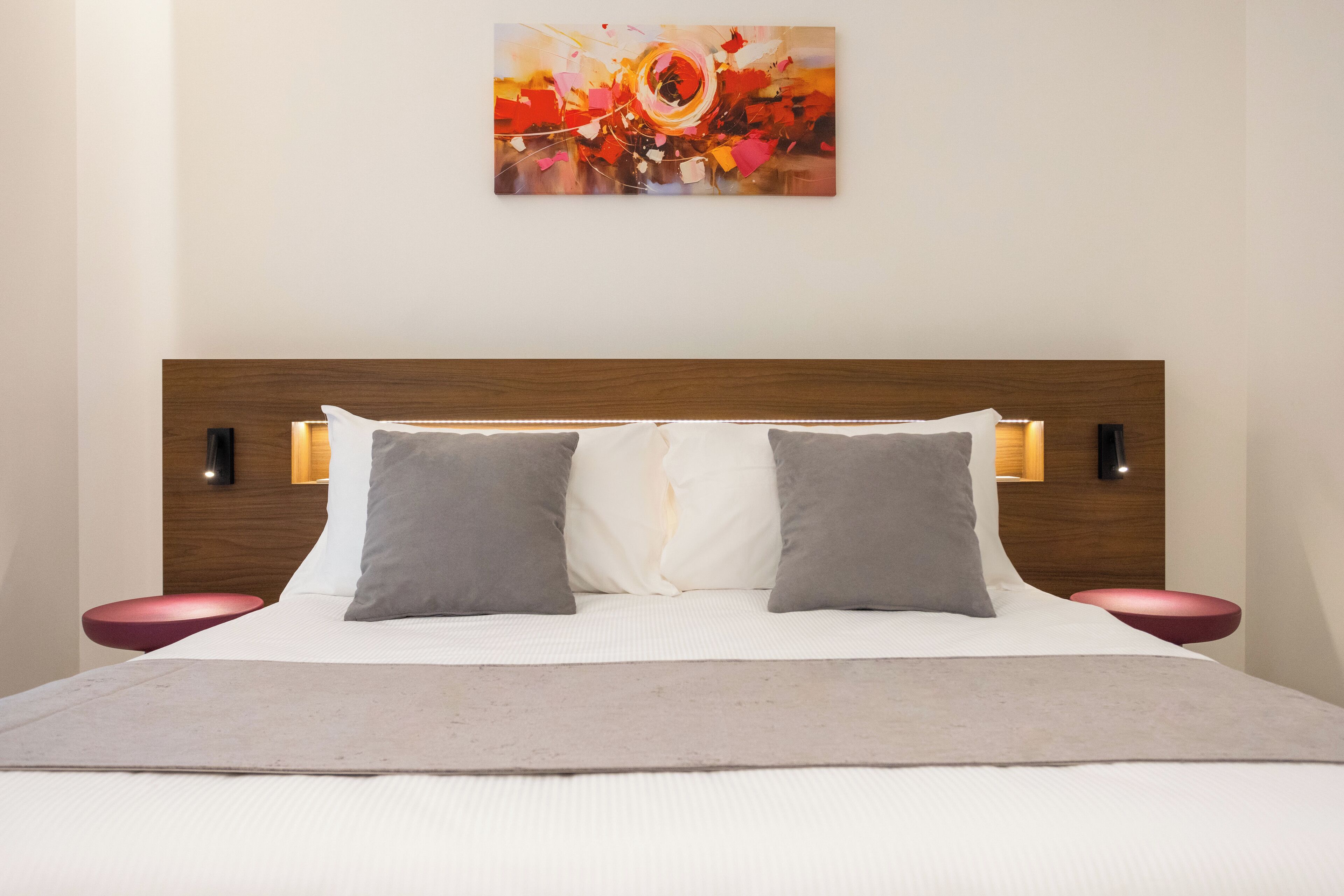 A modern hotel room with a large bed, two bedside tables, and a wall-mounted artwork.