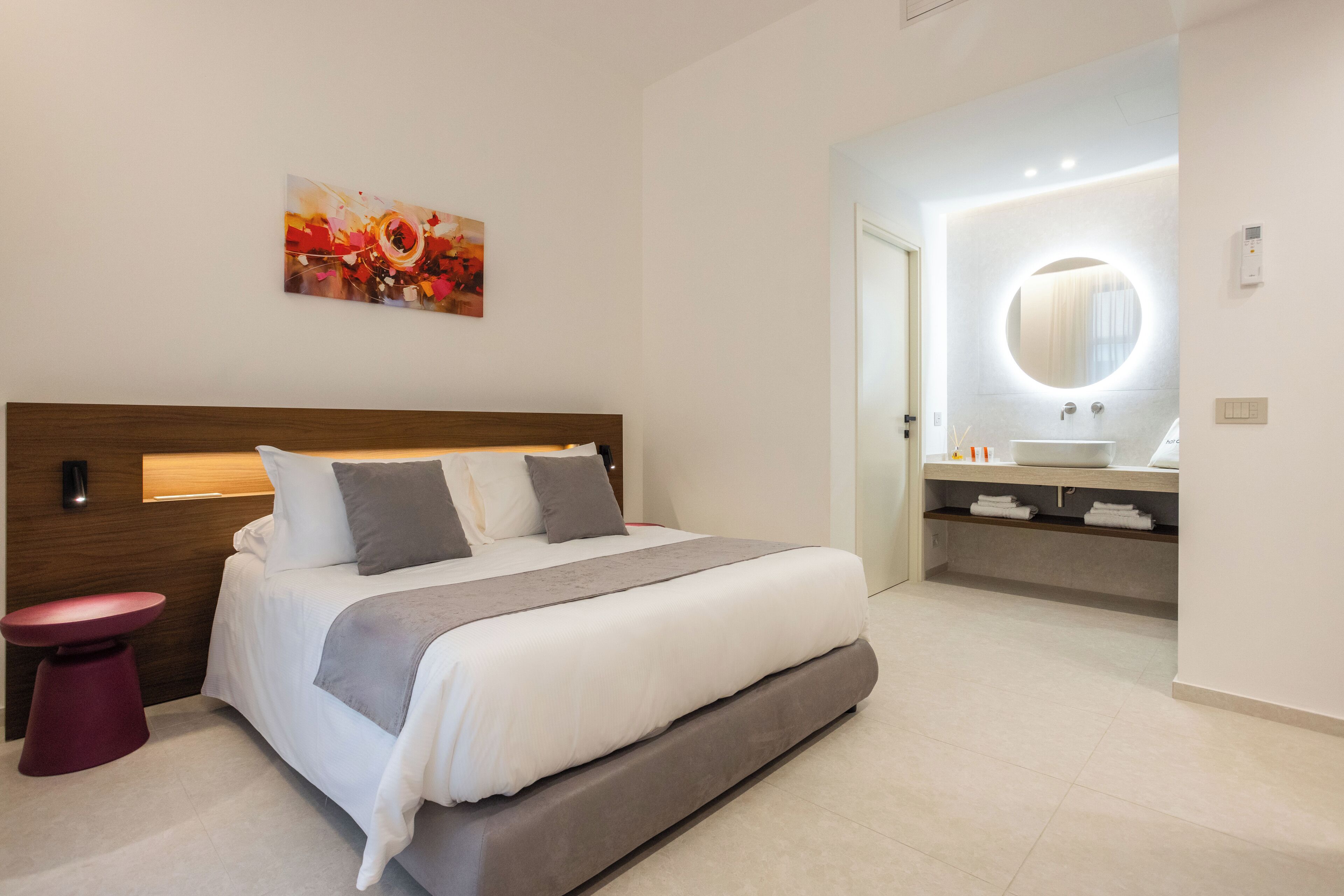 A modern bedroom with a large bed, a bedside table, and a bathroom with a mirror and sink.