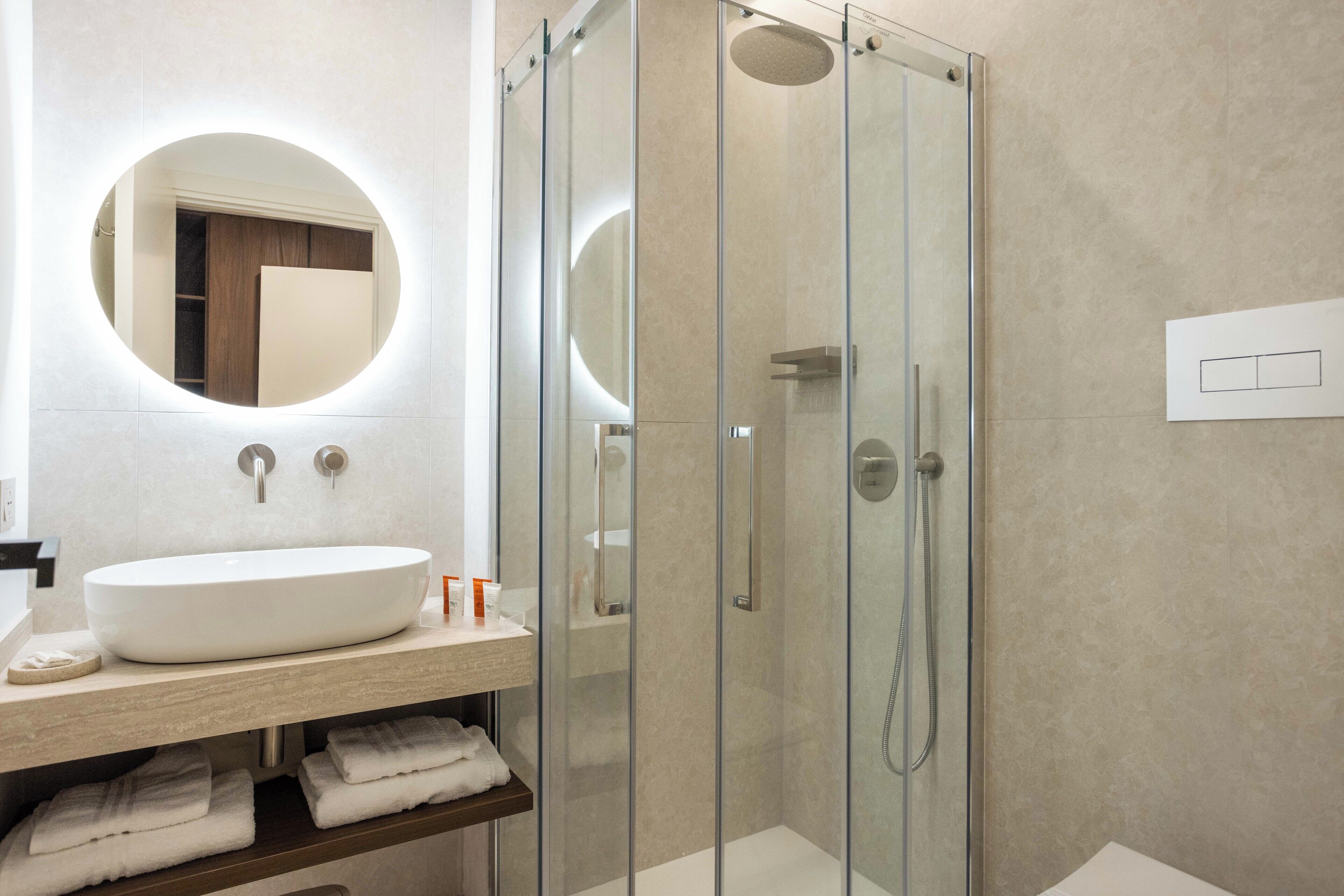 A modern bathroom with a glass-enclosed shower, a round mirror, and a white sink.