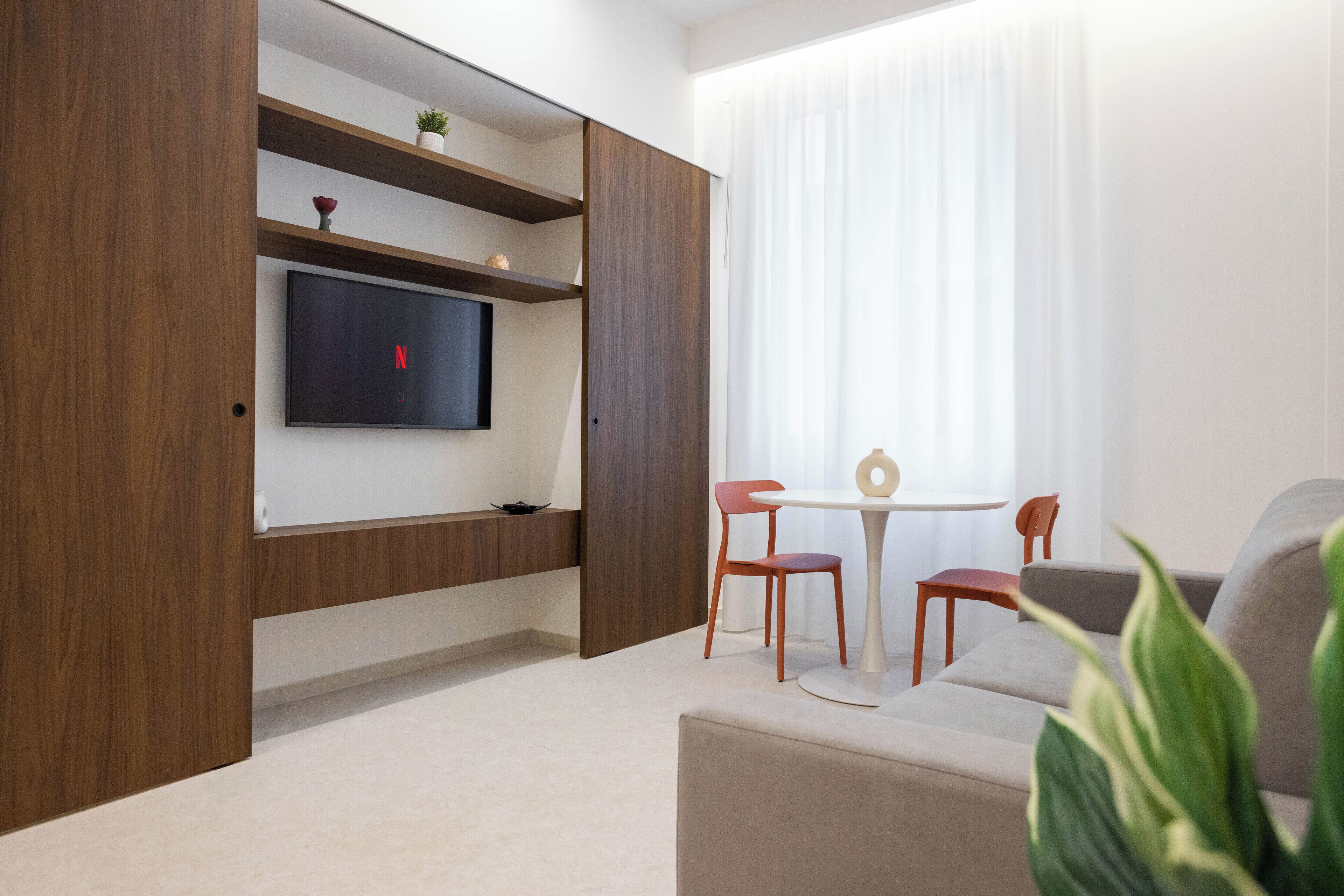Ein modernes Wohnzimmer mit einem an der Holzwand befestigten Flachbildfernseher, einem kleinen Tisch mit zwei Stühlen und einem Sofa.