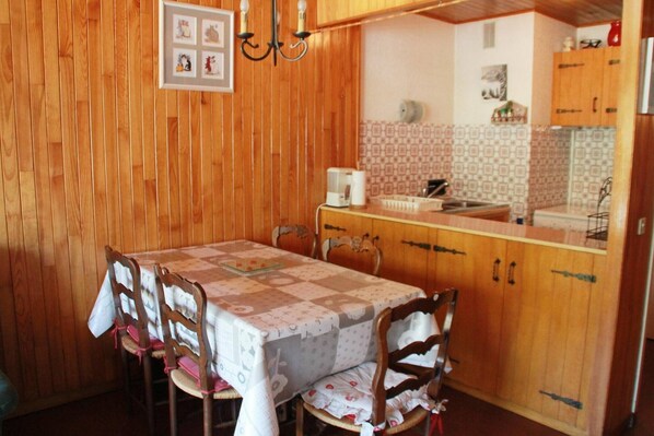 A wooden-paneled dining area with a table set for four, wooden chairs, and a kitchen with patterned tiles and wooden cabinets. - Apartment for 5 people with pool (Châtel)