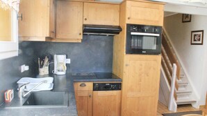 A compact kitchen with wooden cabinets, a dishwasher, a stove, and a microwave. - Apartment in Châtel near Aquatic Centre (Châtel)