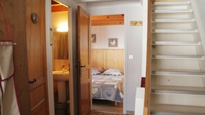 A bedroom with a wooden headboard, a bed with a patterned bedspread, a wooden door, and a white wall with a small picture. - Apartment in Châtel near Aquatic Centre (Châtel)