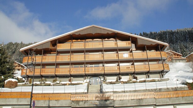 A multi-story building with balconies, a snow-covered roof, and a clear sky. - Apartment in Châtel near Aquatic Centre (Châtel)