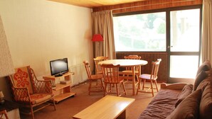 A cozy living room with a wooden table, chairs, a sofa, a television, and a window with curtains. - Apartment only 50 m from the ski slopes (Châtel)