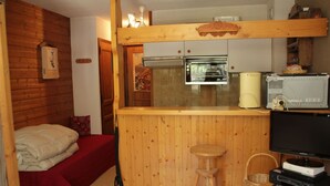 A compact room with a bed, a small kitchenette, a wooden bar area, and a television.