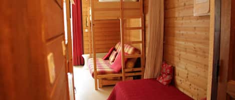 A wooden cabin room with bunk beds, a red curtain, and a framed picture on the wall.