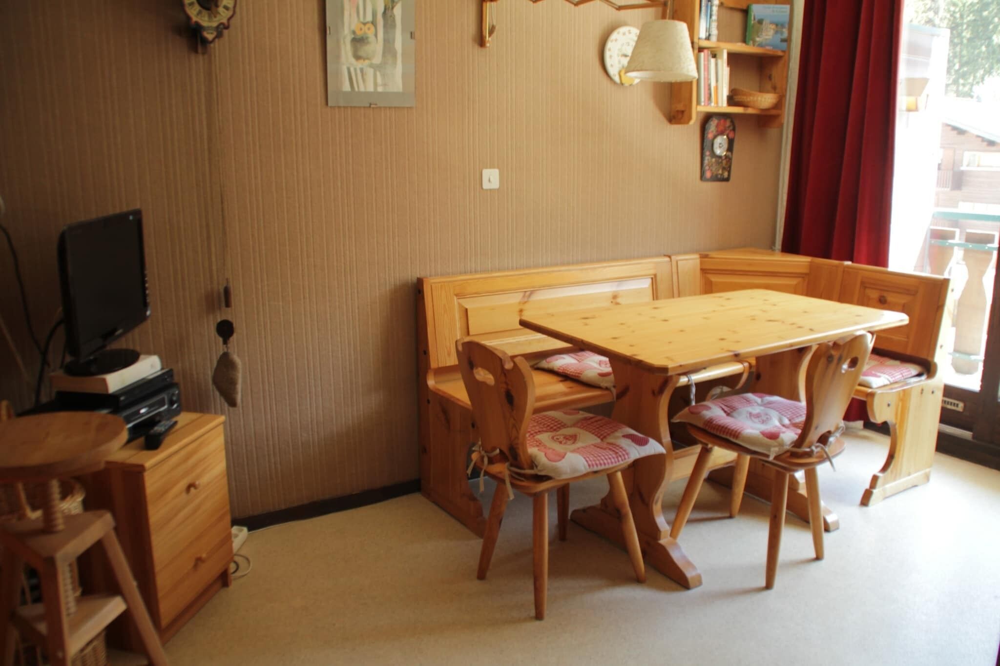 Una habitación acogedora con una mesa de comedor de madera, sillas a juego, un televisor y una estantería.