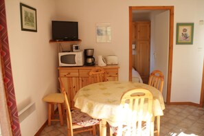 A small dining area with a table, chairs, a microwave, a coffee maker, and a television on a shelf.