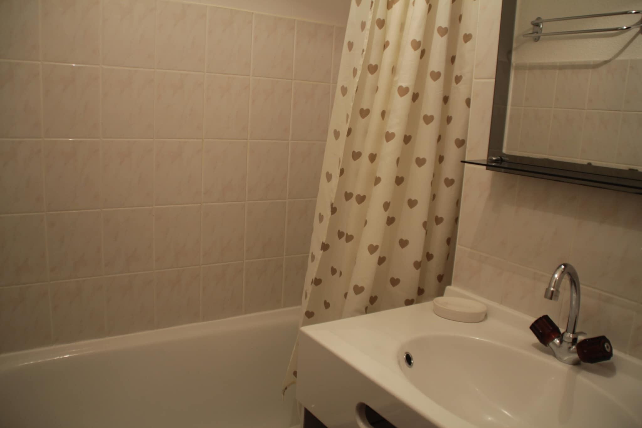 A bathroom with a bathtub, a sink with a soap dish, and a shower curtain with a heart pattern.