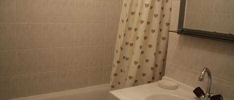 A bathroom with a bathtub, a sink with a soap dish, and a shower curtain with a heart pattern.