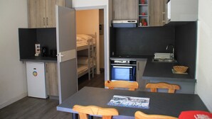 A compact kitchenette with a refrigerator, microwave, and oven. There is a small fridge, a dining table with chairs, and a bunk bed in the background. - Apartment in Chatel near cable car (Châtel)