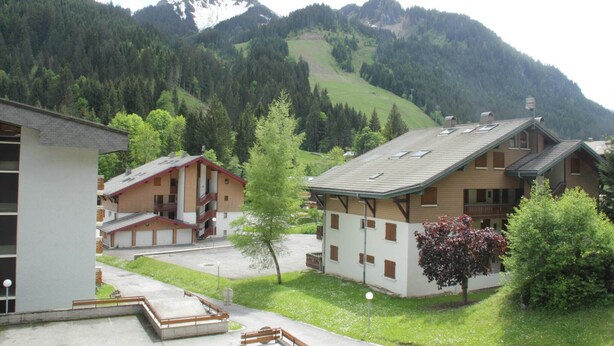 A mountain village with traditional chalet-style buildings, a paved courtyard, and a backdrop of forested hills. - Apartment in Chatel near cable car (Châtel)