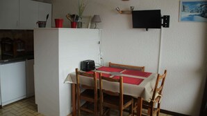 Una cuina petita amb taula i cadires, un rellotge a la paret, i un televisor penjat sobre la taula.
