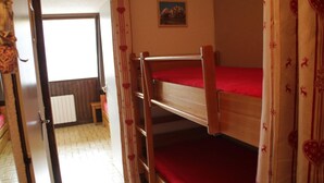 Habitació amb un llit superposat, matalàs vermell, una porta de fusta, un radiador i un quadre petit a la paret.