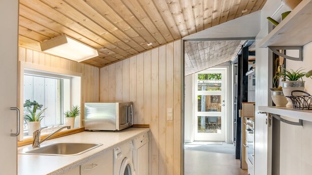 Una cocina moderna con paneles de madera, lavadora integrada, microondas y ventana con plantas en macetas.