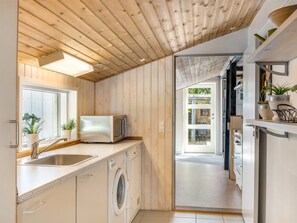Une cuisine moderne avec un lambris en bois, un lave-linge encastré, un four à micro-ondes et une fenêtre agrémentée de plantes en pot.