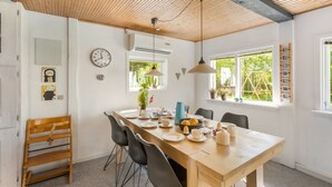 Un comedor con una mesa de madera, sillas, un reloj y una ventana con vistas a follaje.