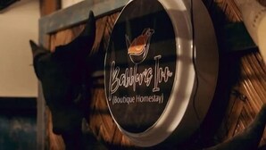 A round, metallic sign with a bird logo and the text "Babblers Inn Boutique Homestay" mounted on a wooden structure. - Babblers Inn By GRB (Tinsukia)