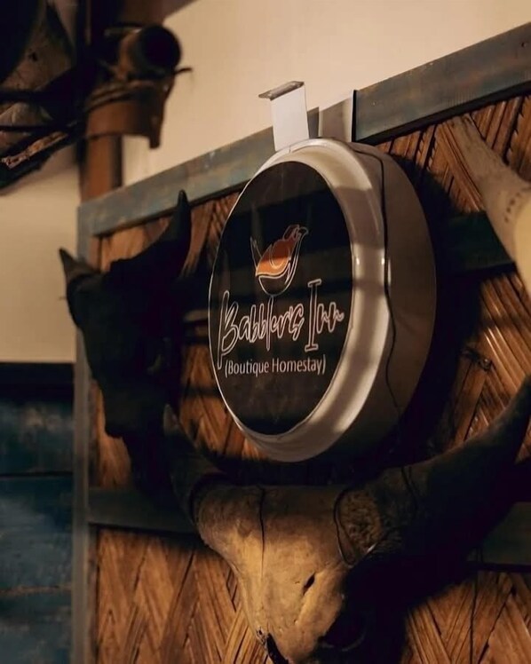 A round, metallic sign with a bird logo and the text "Babblers Inn Boutique Homestay" mounted on a wooden structure. - Babblers Inn By GRB (Tinsukia)