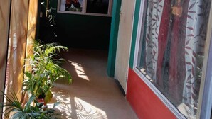 A narrow hallway with potted plants on one side and a large window with patterned curtains on the other. - Babblers Inn By GRB (Tinsukia)