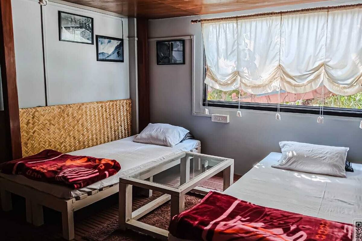 Uma cabana com duas camas, uma mesa pequena e uma janela com cortinas.