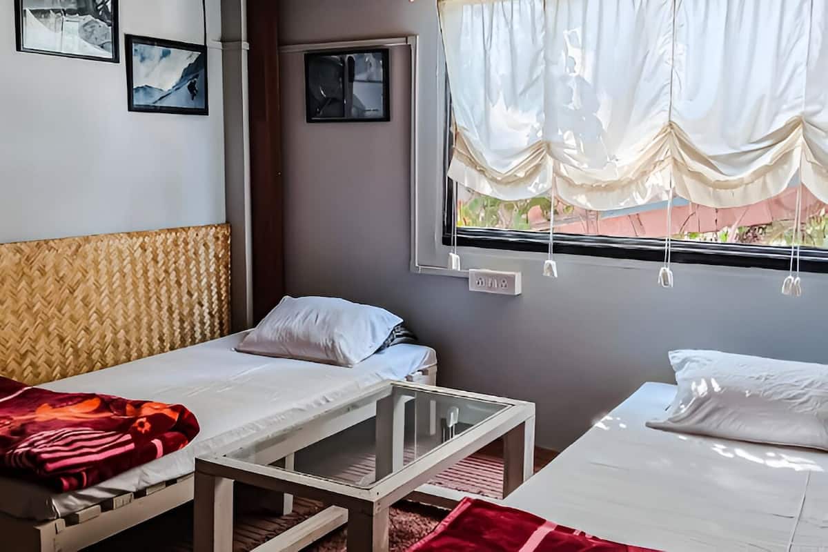 Quarto com duas camas, uma mesa pequena e uma janela com cortinas.
