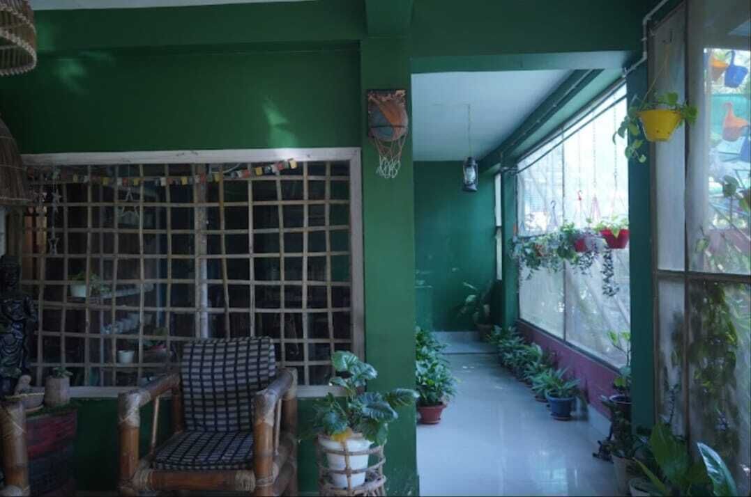 A covered outdoor area with a wooden chair, potted plants, and a window with a grid pattern.