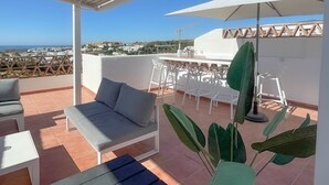 A rooftop terrace with a white table and chairs, a grey sofa, and a large umbrella. - Luxe Golf & Family House Escape (Estepona)
